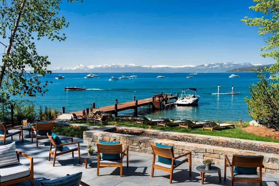 Lakeside resort patio with wooden chairs overlooking boats, mountains, and snowy peaks