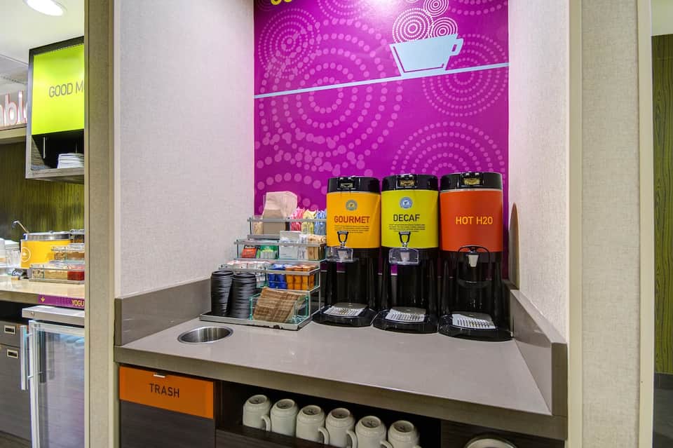 Modern hotel coffee station with vibrant purple accent wall and three beverage dispensers