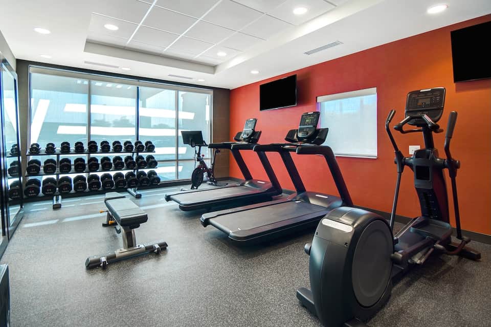 Modern fitness center with treadmills, exercise equipment, dumbbells, and orange accent walls