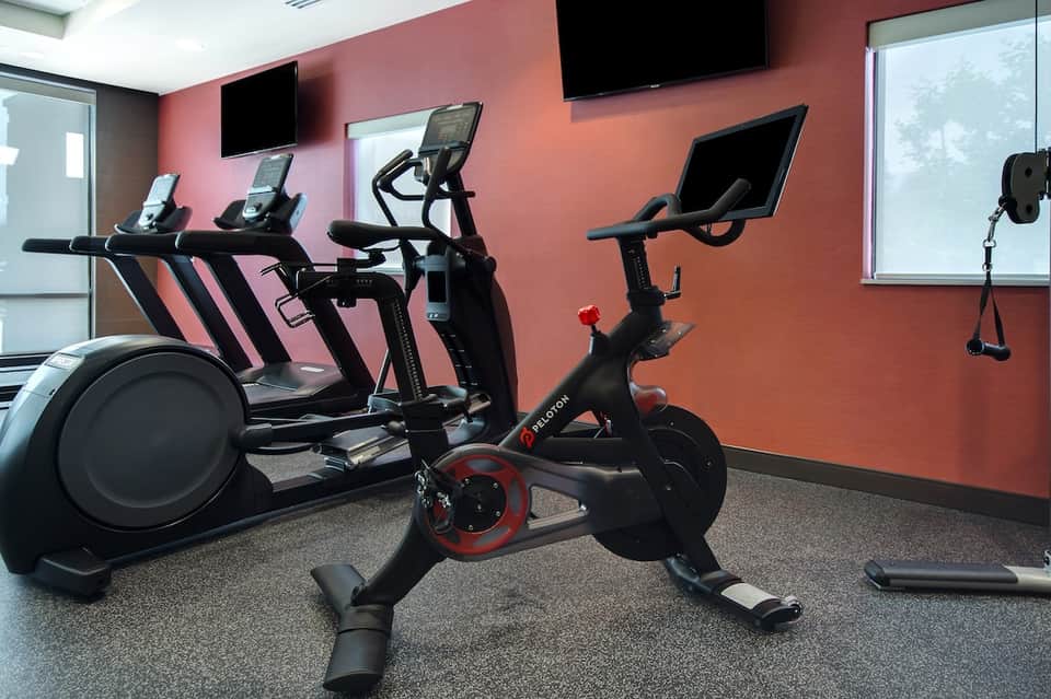 Fitness center with red wall, stationary bikes, elliptical machine, and TV screens