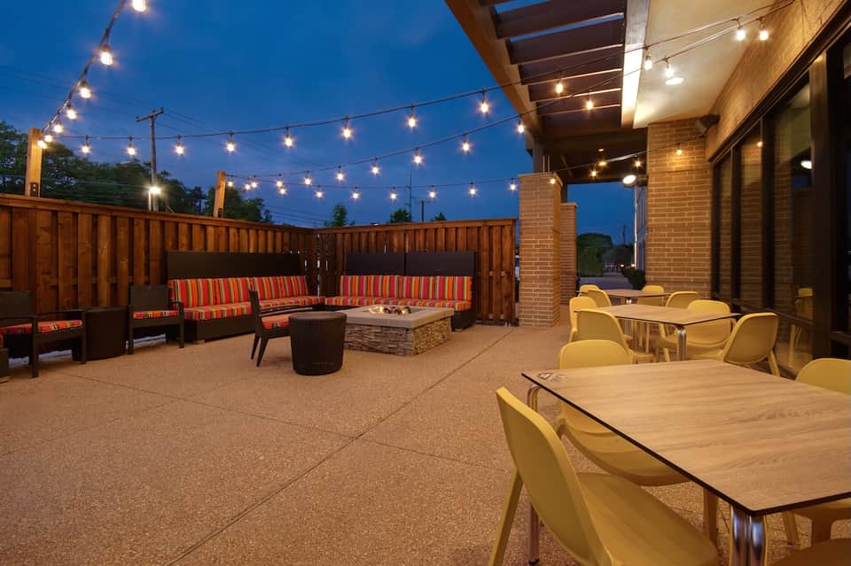 Evening patio with string lights, fire pit, striped orange seating, and dining tables