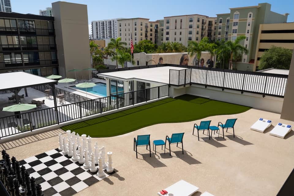 Resort rooftop terrace with pool, artificial lawn, chess game setup, and city views