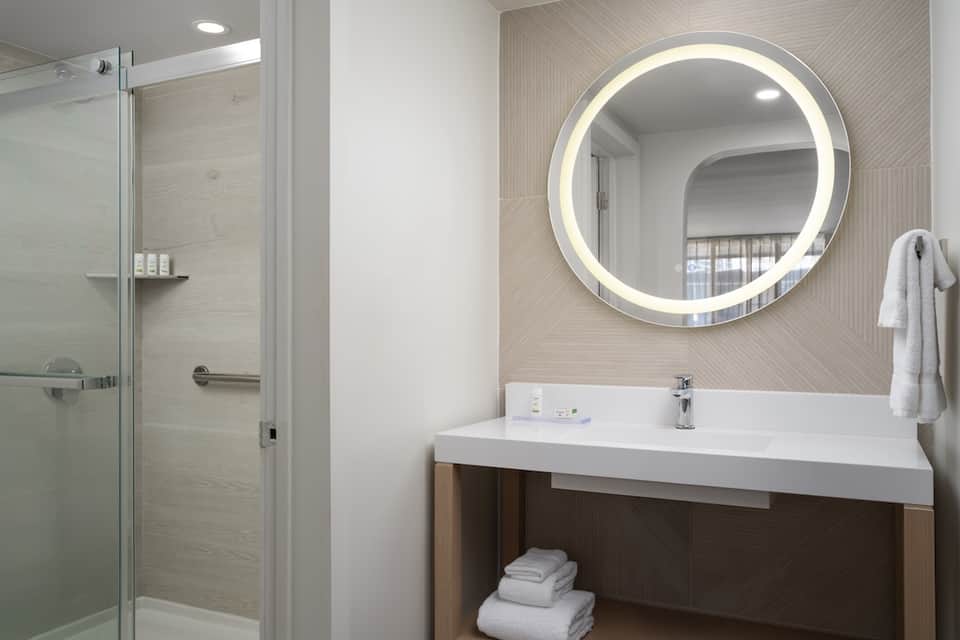 Modern bathroom with illuminated circular mirror, walk-in shower, and neutral tones