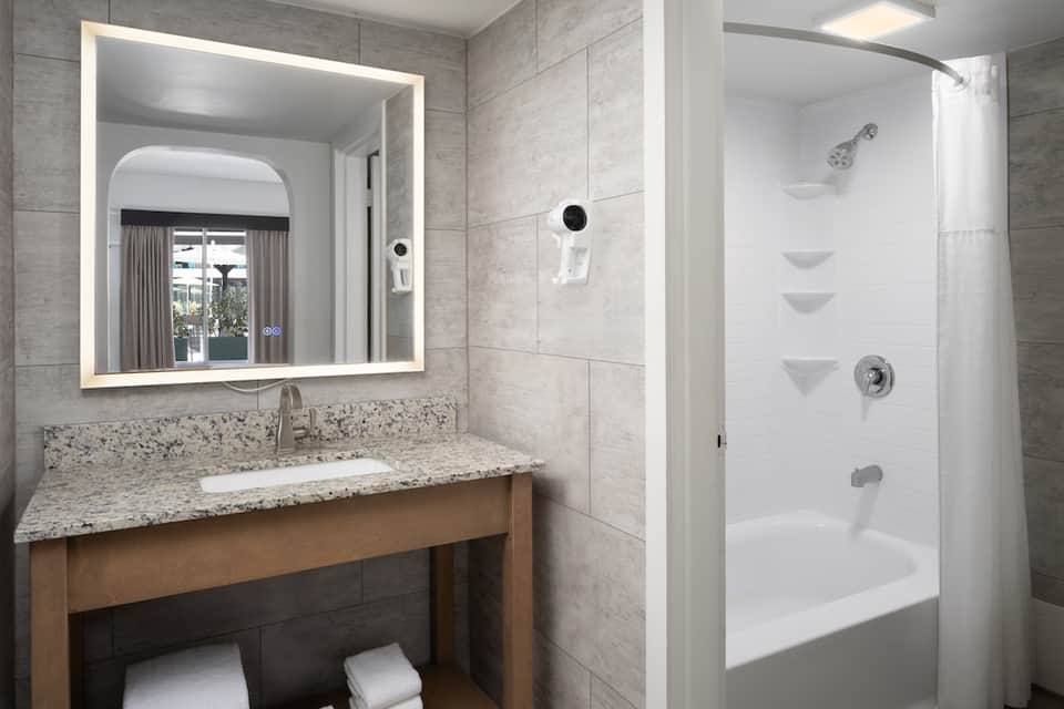 Modern hotel bathroom with granite countertop, lit mirror, and walk-in shower