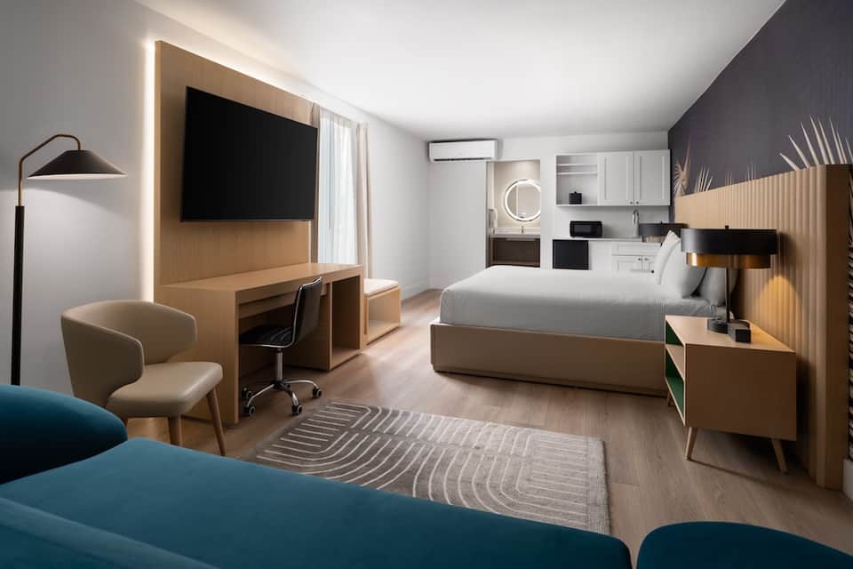 Contemporary hotel room with queen bed, wooden accents, work desk, flat-screen TV, and modern bathroom
