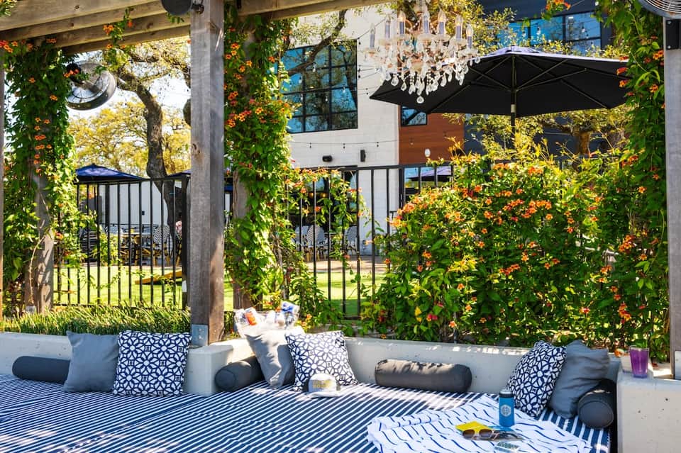 Outdoor lounge area with white seating, striped cushions, flowering vines, black umbrella and lights