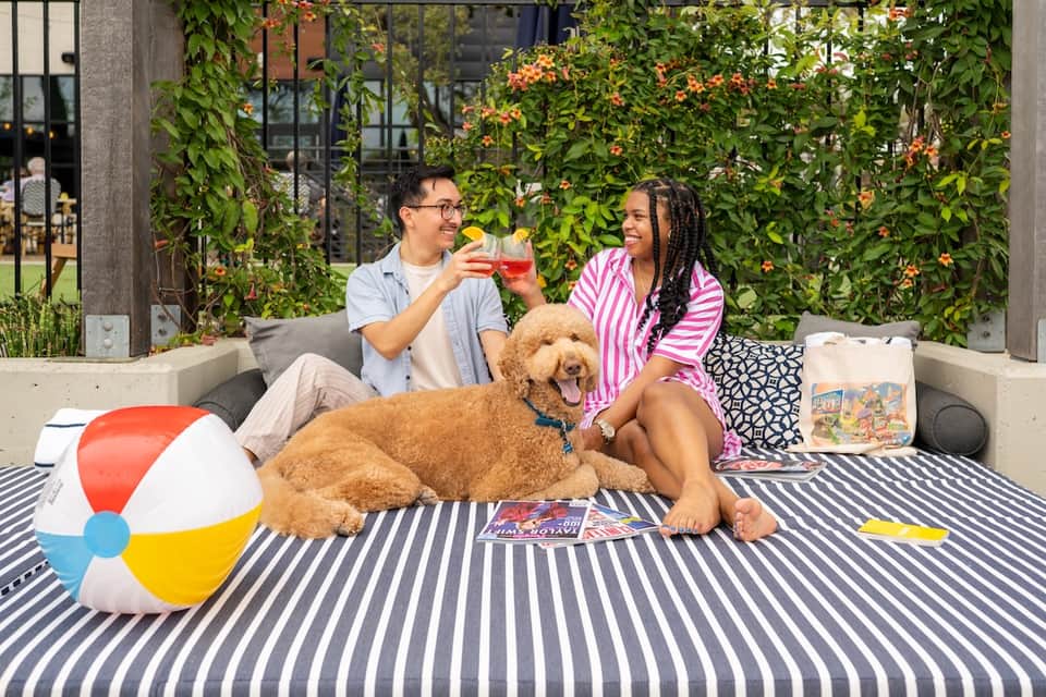 Couple with dog enjoying drinks on outdoor patio with flowering vines and seating