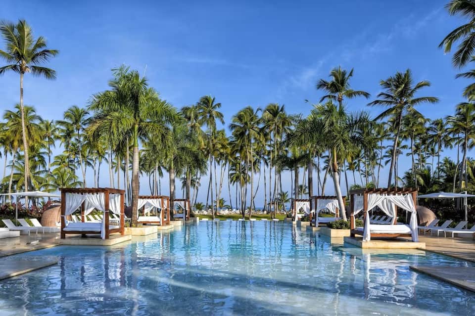 Luxury resort pool with cabanas, white drapes, palm trees, and tropical landscaping