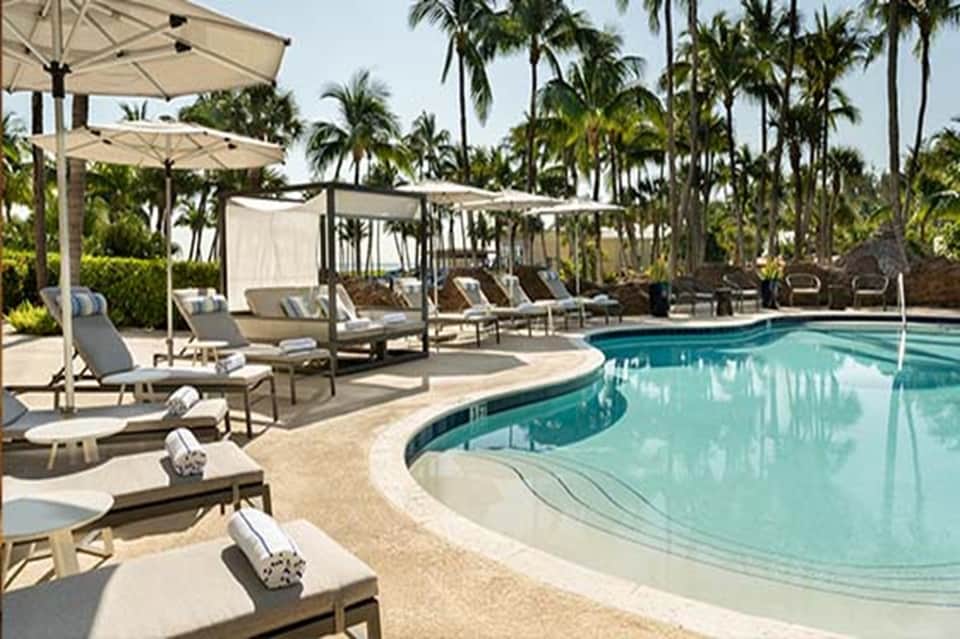 Resort swimming pool surrounded by lounge chairs, umbrellas, and tropical palm trees