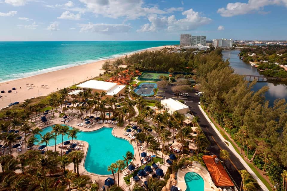 Beachfront resort aerial view with curved pool, palm trees, pristine beach, and waterfront location