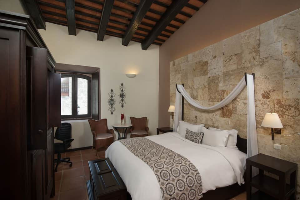 Rustic bedroom with stone accent wall, canopy bed, dark wood beams, and traditional decor