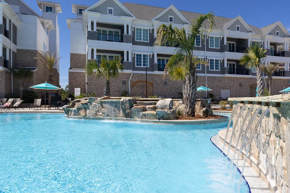 Luxury waterfront resort with white buildings, decorative pool with rock features, and palm trees