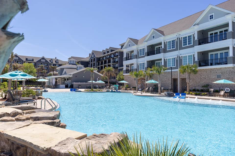 Resort pool with turquoise water, palm trees, and multi-story apartment buildings