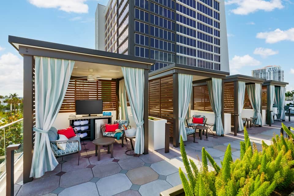 Urban rooftop cabanas with white curtains, wooden slats, and city skyline views