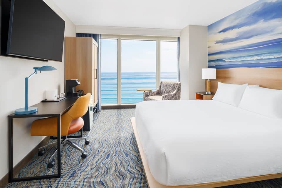 Beachfront hotel room with ocean view balcony, desk workspace, and modern furnishings