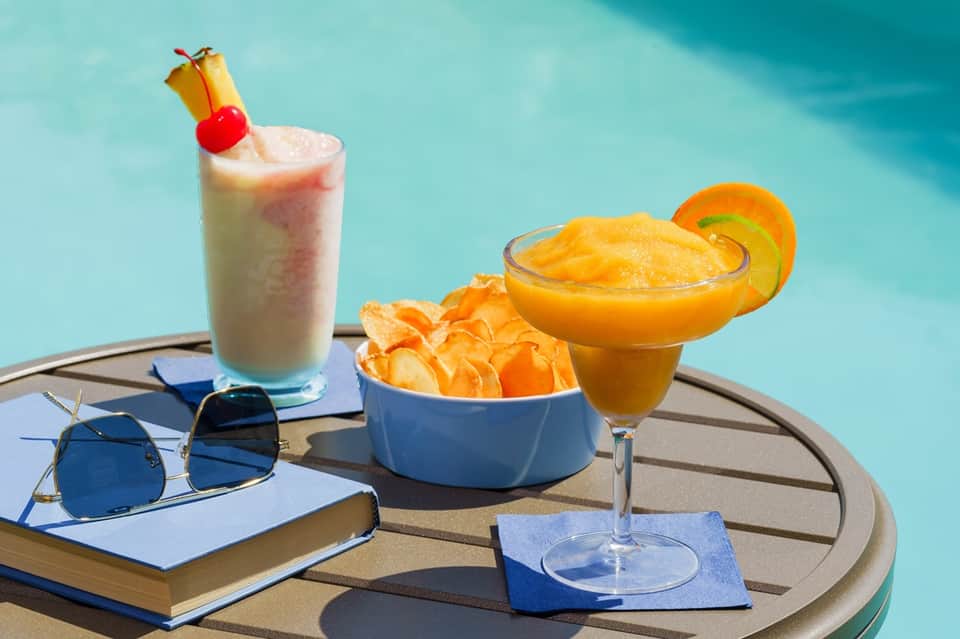 Tropical cocktails and appetizers poolside with sunglasses and book on table