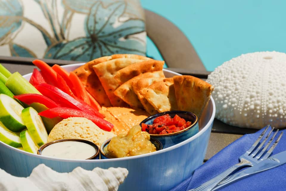 Beachside appetizer plate with fried items, fresh vegetables, and dipping sauces on blue napkin