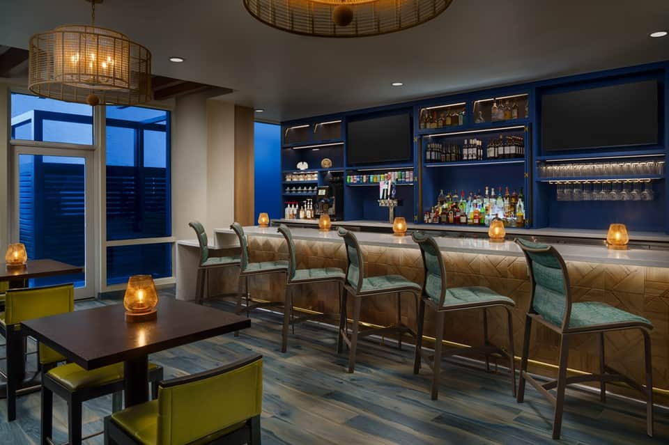 Modern hotel bar with blue walls, gold pendant lights, leather seating, and full liquor shelves