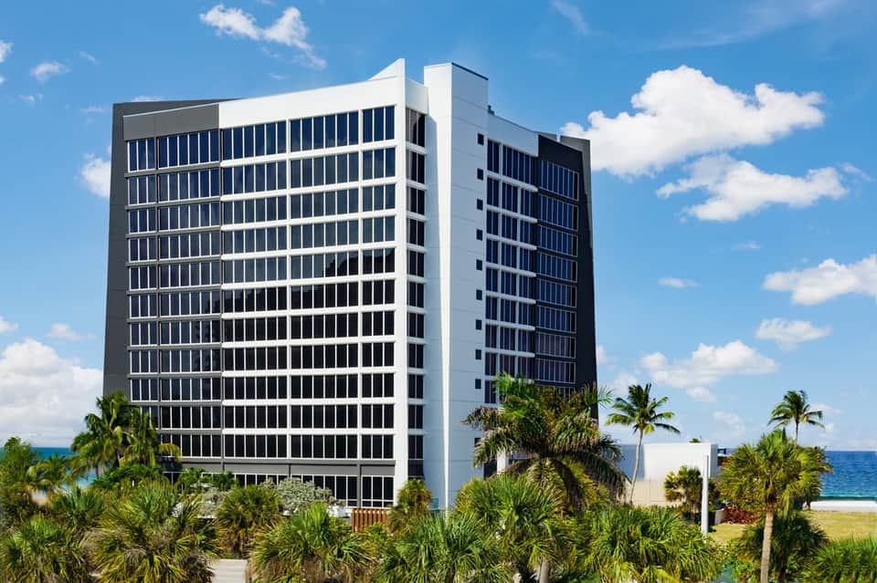 Tall white and dark blue beachfront hotel building with palm trees and ocean view