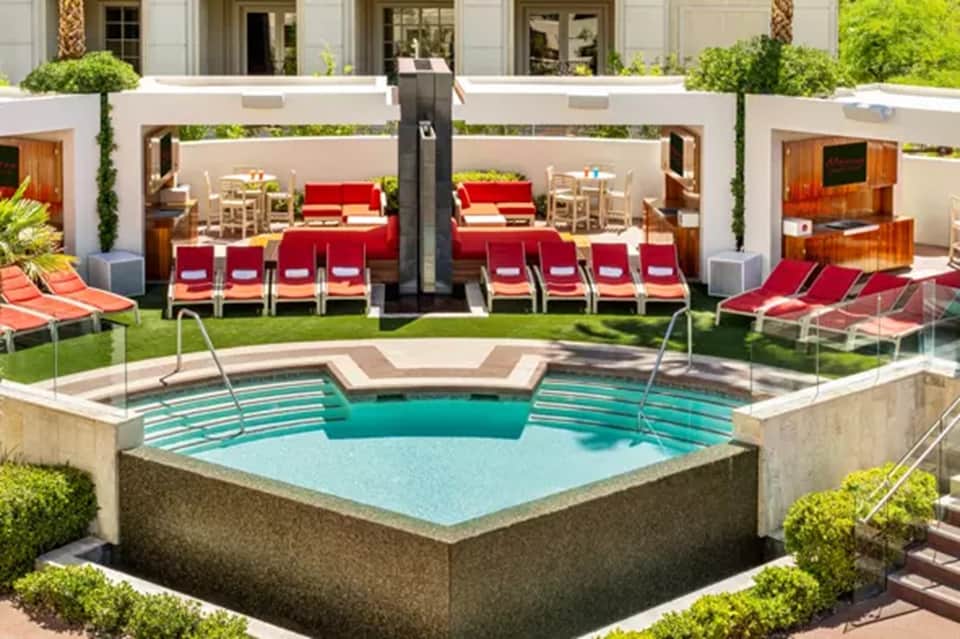 Luxurious outdoor pool with sunbathing area, red lounge chairs, white umbrellas, and modern architecture