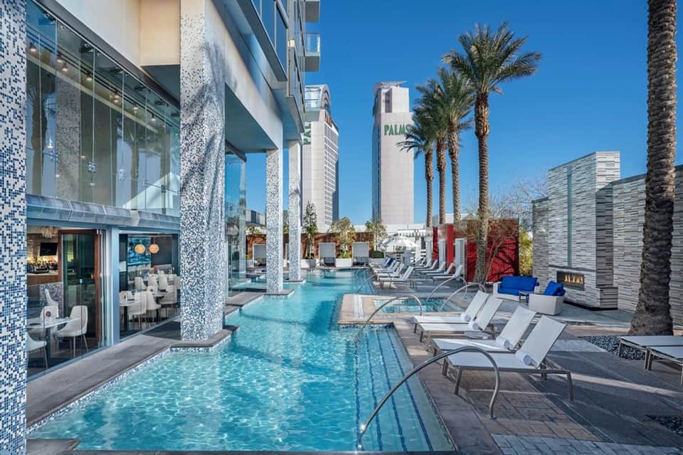 Modern resort pool deck with blue water, loungers, palm trees, and contemporary architecture