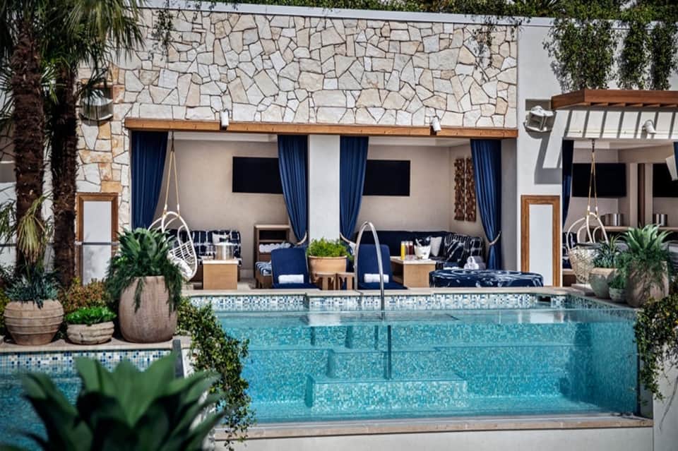 Modern pool cabana with hanging chairs, blue curtains, and stone accent wall