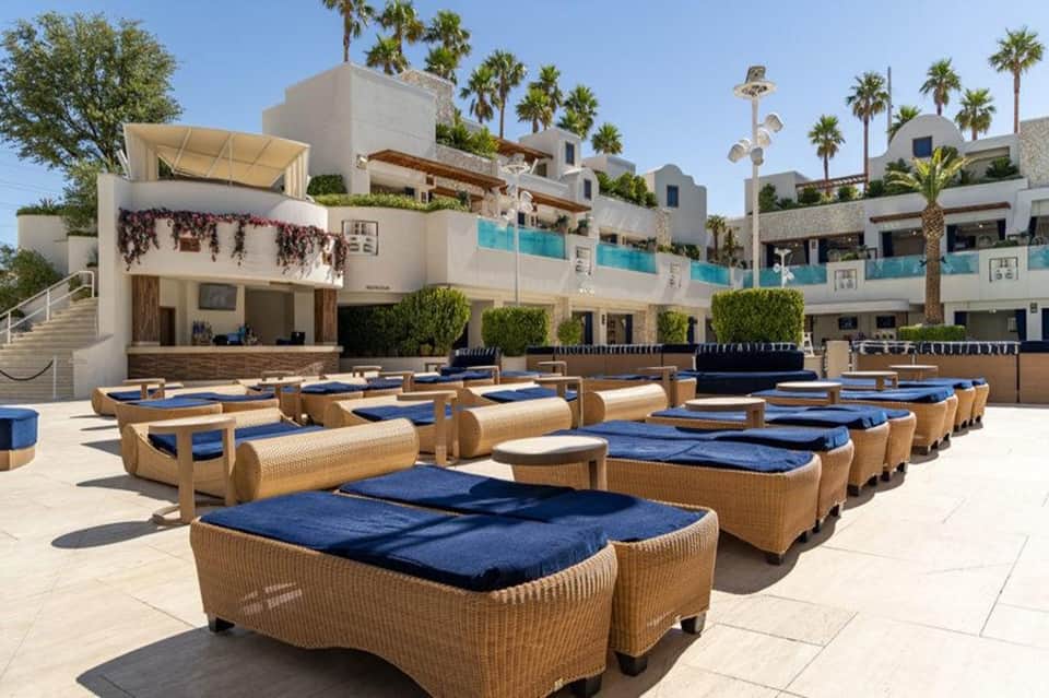 Beachfront resort lounge area with woven furniture, blue cushions, and white buildings