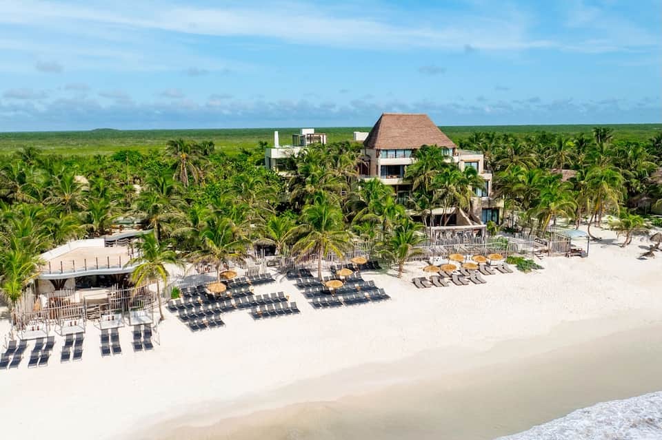 Luxury beachfront property with thatched-roof structure and lounge chairs on white sand
