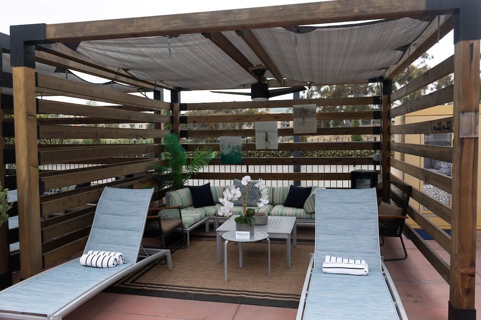 Modern deck with pergola shade structure, lounge chairs, white sofa, and railing overlooking neighborhood