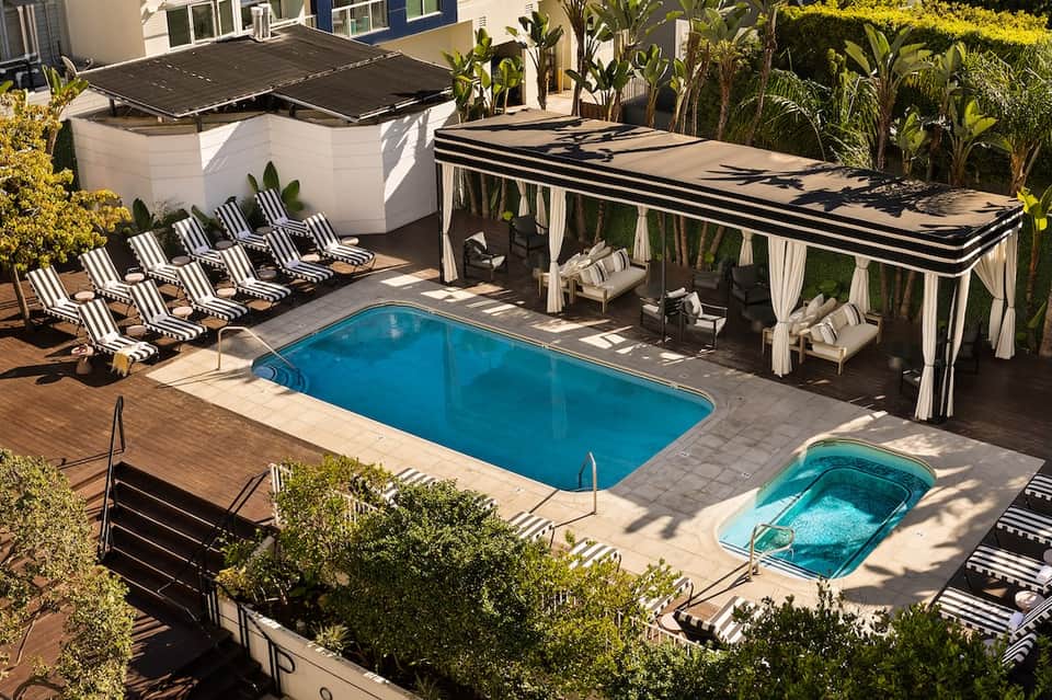 Aerial view of two pools with black and white striped loungers and cabanas