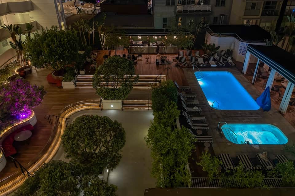 Night view of illuminated resort courtyard with multiple pools, lounge chairs, and surrounding buildings