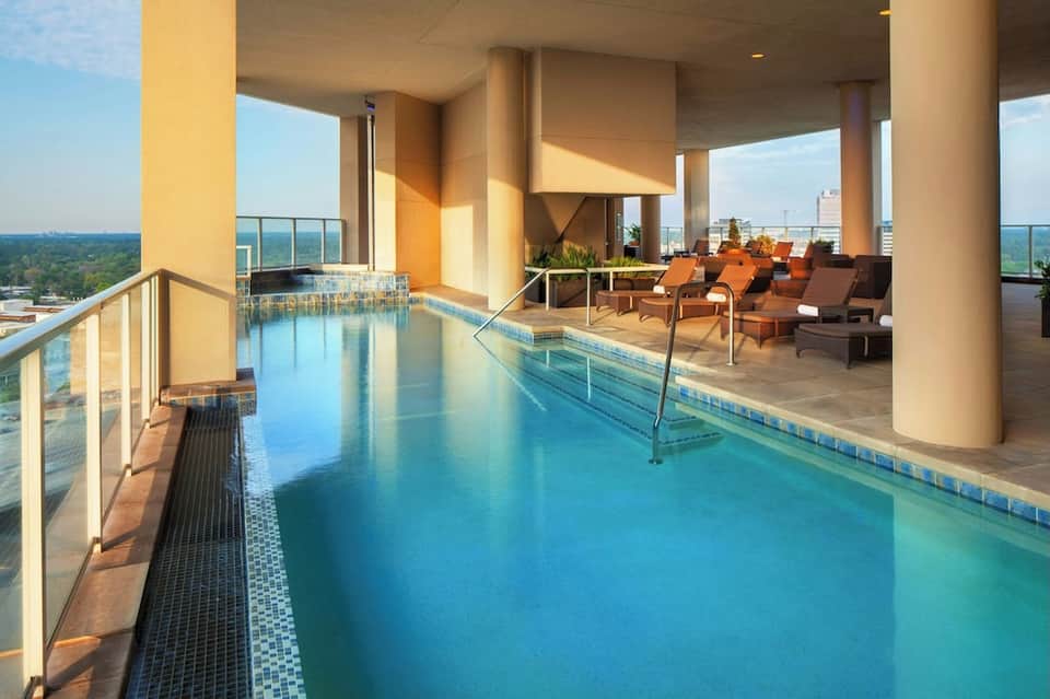 Indoor lap pool with glass railings, lounging area with orange chairs, and large windows with nature views