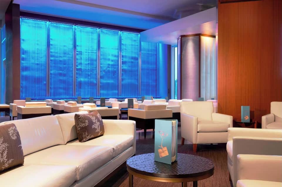 Upscale hotel lounge with cream seating, floor-to-ceiling blue-lit windows, and contemporary design