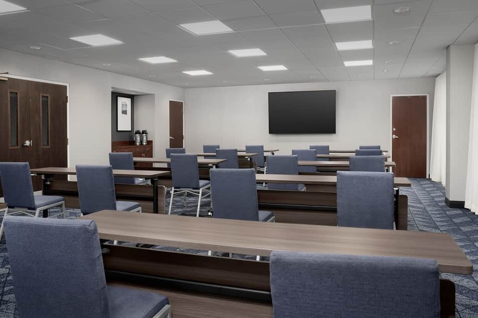 Corporate conference room with long wood table, blue chairs, and wall-mounted screen