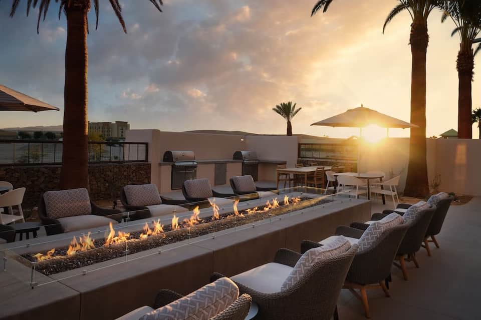 Rooftop terrace with dual linear fire pits, wicker lounge chairs, and sunset desert landscape