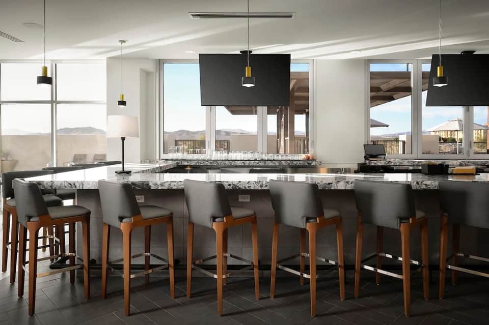 Modern bar lounge with granite countertops, wooden bar stools, panoramic windows with mountain views