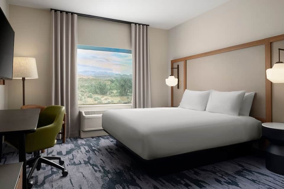 Upscale hotel room with queen bed, work desk, large window overlooking desert landscape