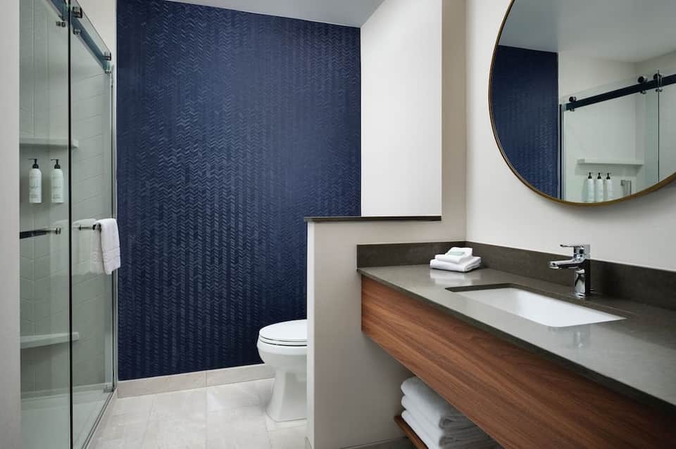 Modern bathroom with dark herringbone tile accent wall, floating vanity, and glass shower