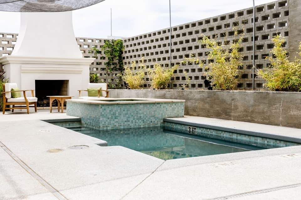 Residential rooftop with sunken pool, modern fireplace, concrete walls, and landscape background