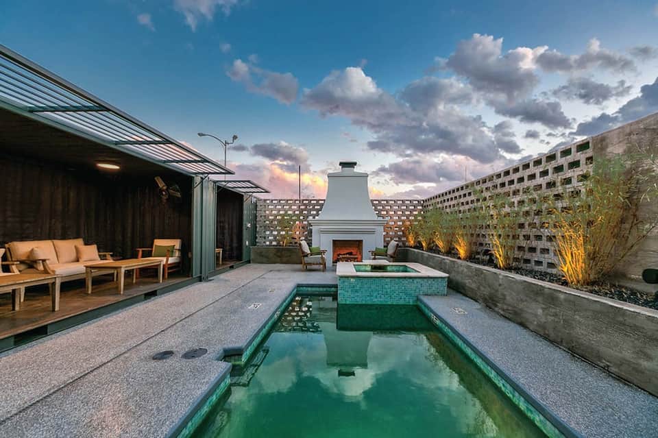 Rooftop infinity pool with fireplace, modern seating, and multi-story building backdrop at twilight