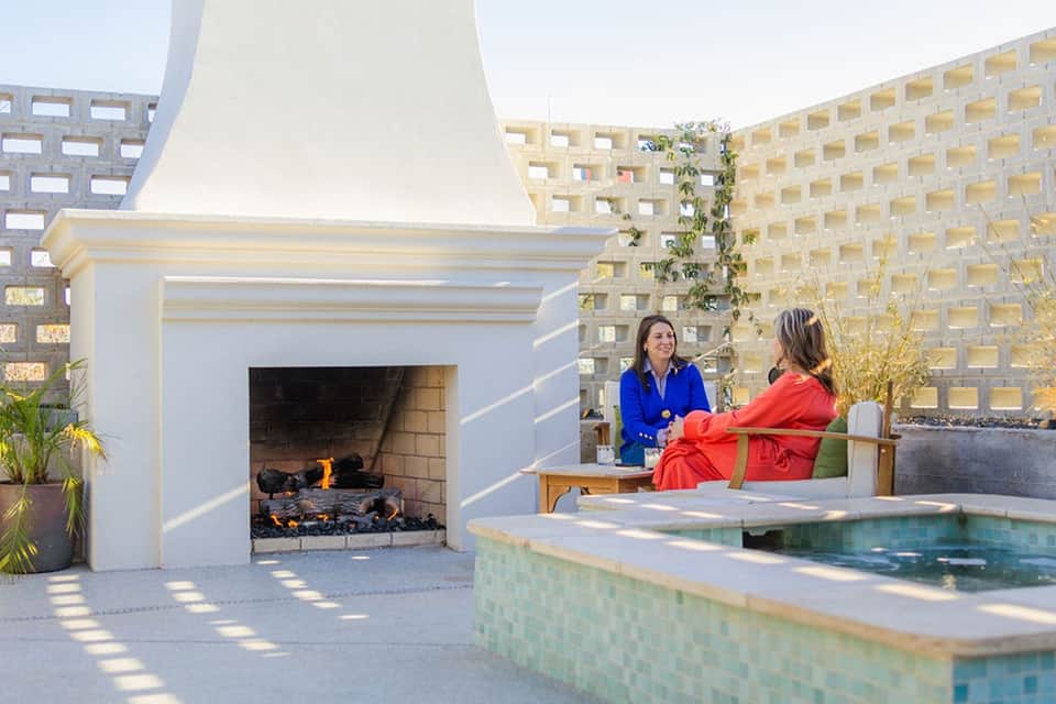 Rooftop fireplace lounge with white architectural features, two women conversing, and water feature
