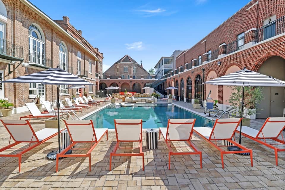 Indoor pool surrounded by brick historic buildings with lounge chairs and striped umbrellas