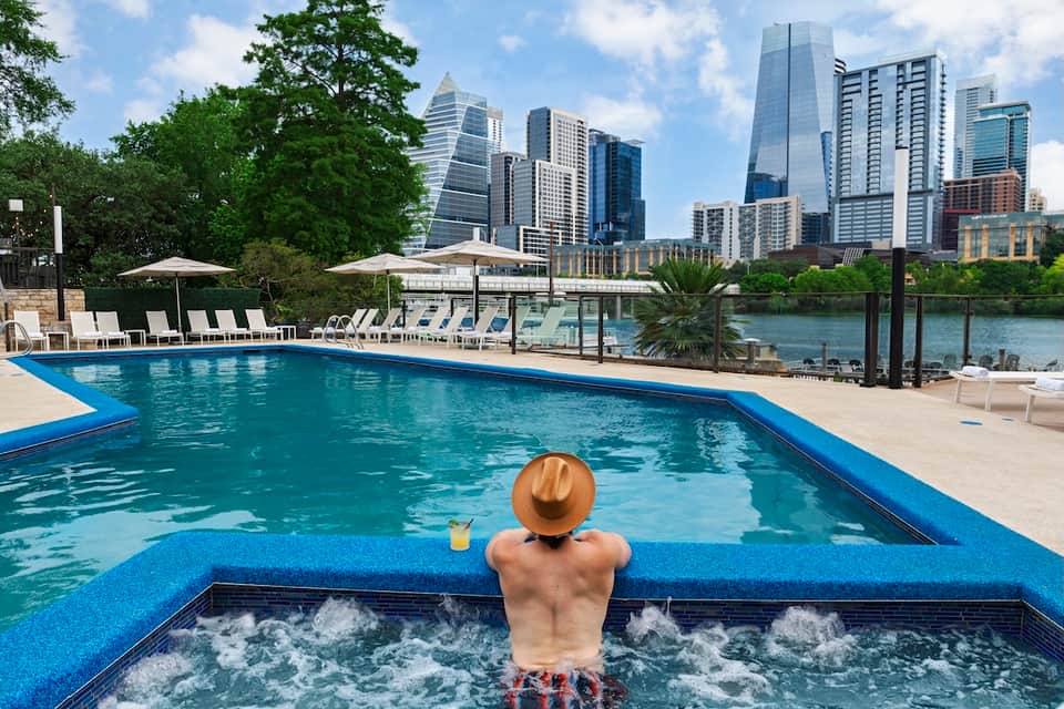 Urban rooftop pool with hot tub, skyline view, and lounge chairs
