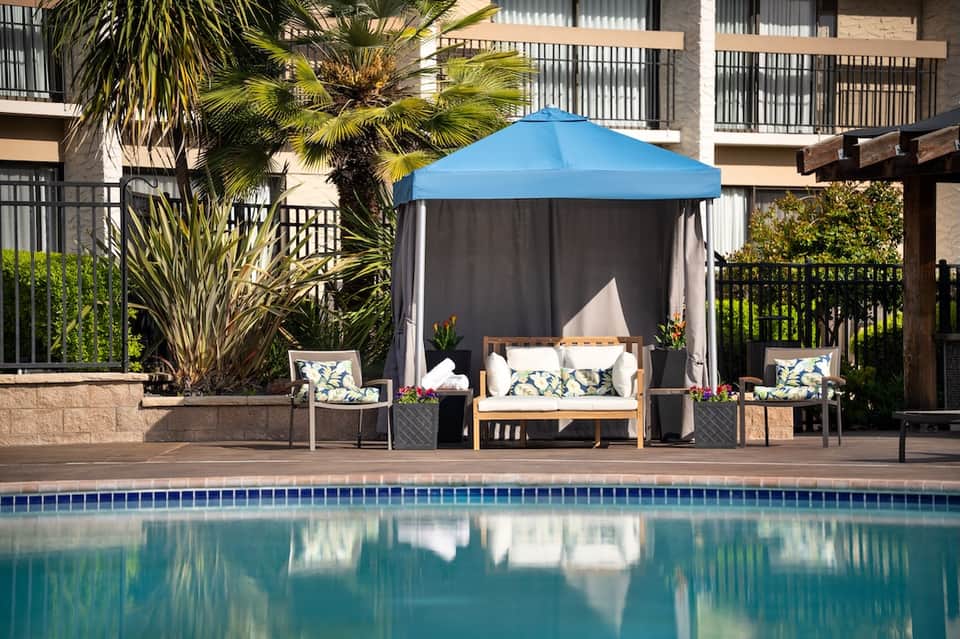 Poolside cabana with blue canopy and lounge seating near apartment complex
