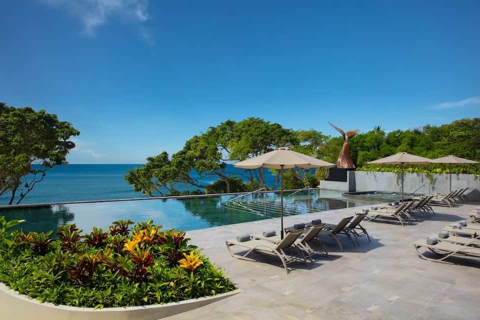 Infinity pool overlooking ocean with tropical vegetation and loungers