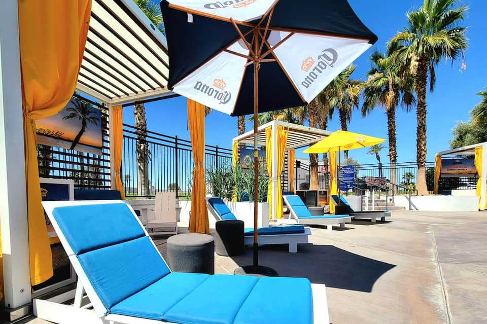 Upscale beachfront pool deck with blue loungers, umbrellas, palm trees, and ocean view on sunny day