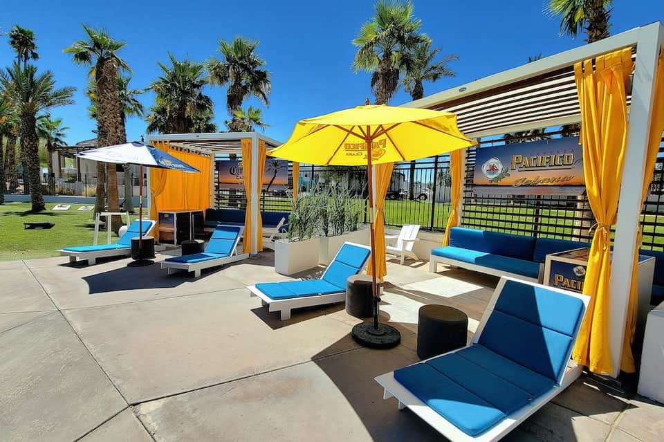 Outdoor pool deck with yellow umbrellas, blue loungers, and palm trees