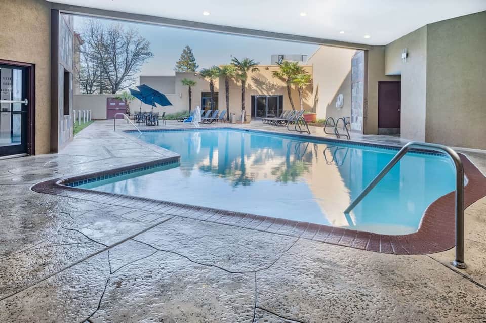 Indoor pool with glass enclosure, lounge chairs, and surrounding building architecture