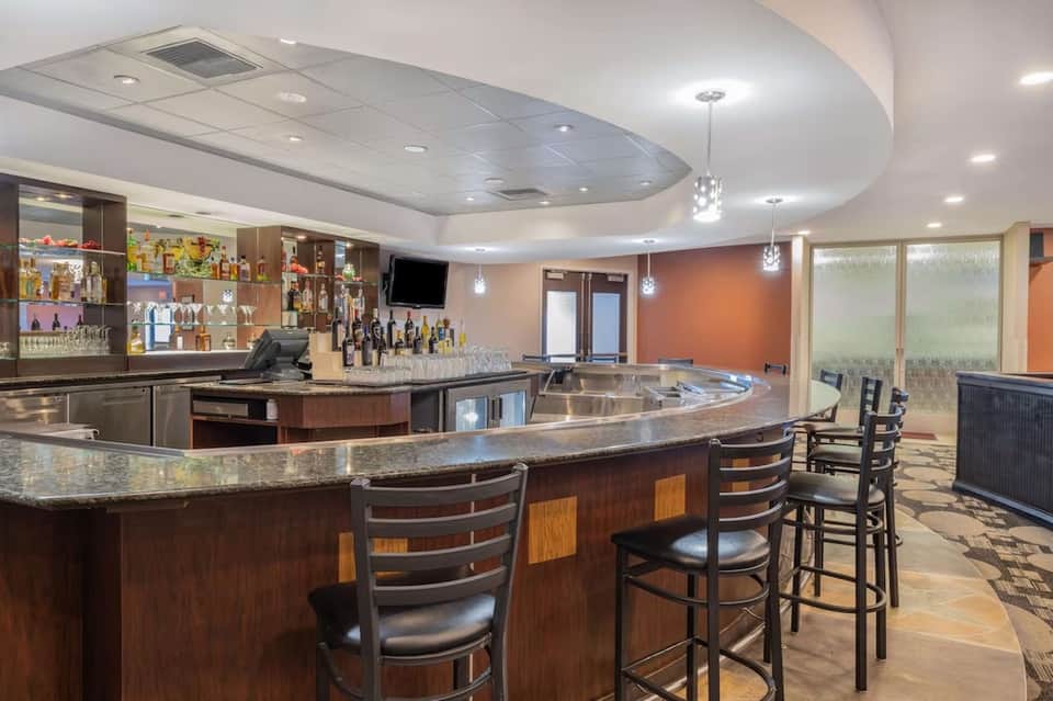 Hotel bar with curved counter, dark wood cabinetry, pendant lighting, and orange accent wall