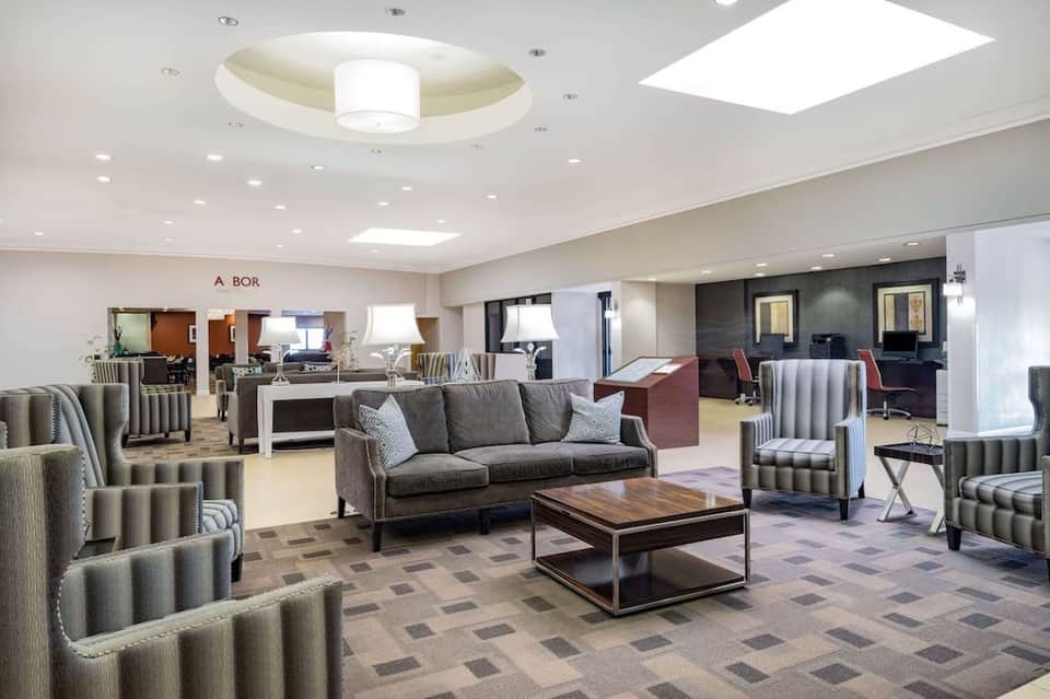 Spacious modern hotel lobby with neutral furnishings, skylight, multiple seating areas, and wayfinding signage
